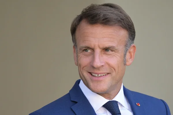 Le président Emmanuel Macron souriant devant un fond neutre.