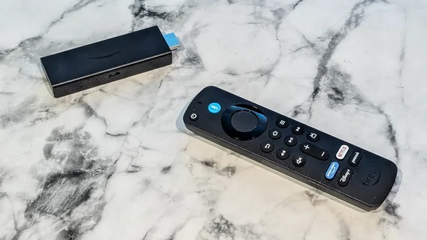 Le Fire TV Stick et sa télécommande disposés sur un marbre blanc avec les raccourcis vers les services de streaming.