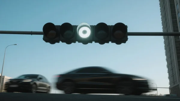 Vue en contre-plongée d'un feu de signalisation urbain moderne affichant un cercle lumineux blanc éclatant, avec des silhouettes de voitures floues circulant en dessous dans une rue de ville contemporaine