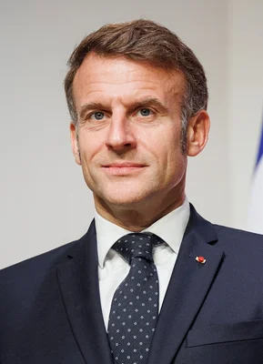 Emmanuel Macron en costume devant un fond neutre et un drapeau.