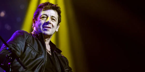 Patrick Bruel sous un projecteur jaune, vêtu d'une veste en cuir.