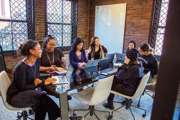 Sept femmes en réunion collaborative autour d'une table en verre dans un espace de travail Match Group.