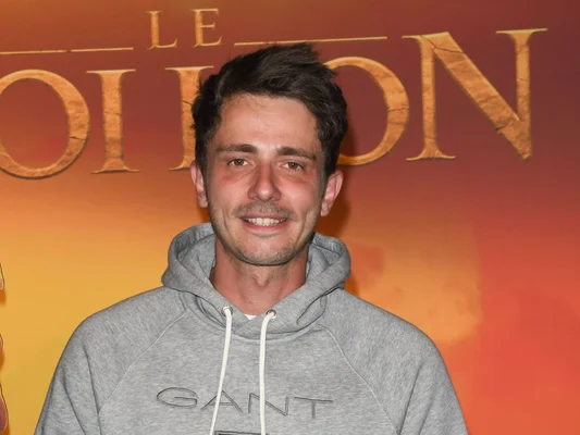 Guillaume Pley en sweat-shirt gris GANT devant un fond doré.