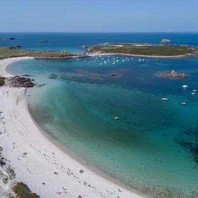 Vue aérienne des eaux turquoises de la mer d'Iroise bordant une plage et une île surmontée d'un phare.