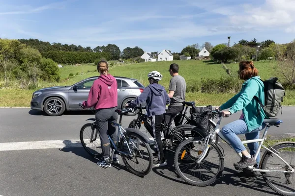 Un groupe de cyclistes et une voiture se partageant une route étroite dans le paysage rural de Belle-Île.