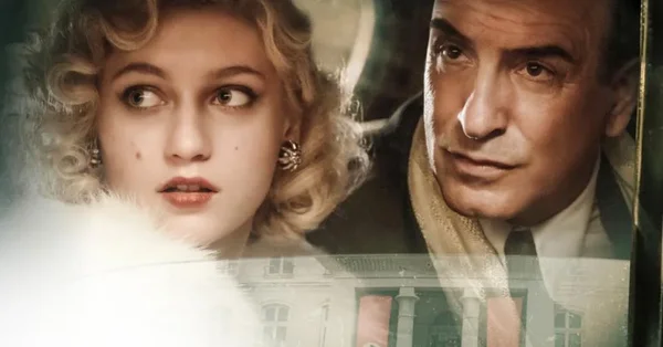 Deux personnages, dont une femme aux cheveux blonds bouclés, posant devant un bâtiment.