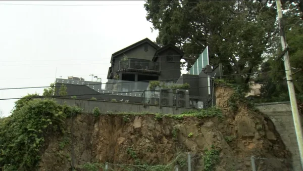 Homme en costume bleu marine et cravate à pois s'exprimant devant un fond rouge.