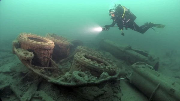 Un plongeur explorant les vestiges rouillés d'une épave posée sur le fond marin.