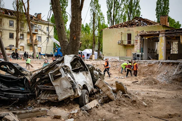 Véhicule détruit et secouristes en gilets de sécurité parmi les décombres d'une zone touchée par les combats en Ukraine.