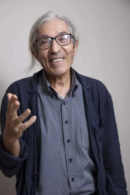 Boualem Sansal souriant et gesticulant devant un fond clair.