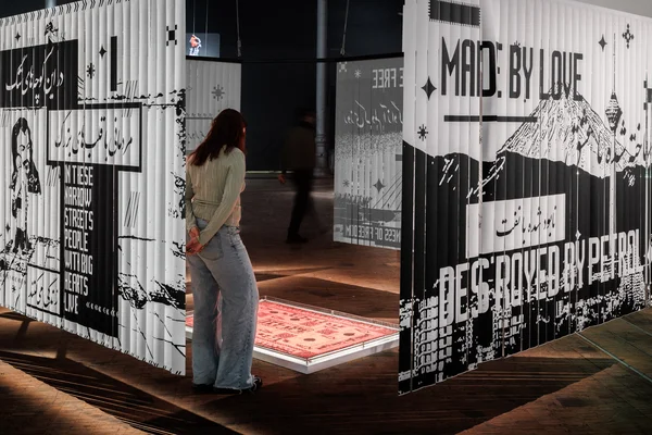 Une visiteuse regardant des œuvres graphiques et textuelles lors de l'exposition 100% L'EXPO à la Grande Halle de la Villette.