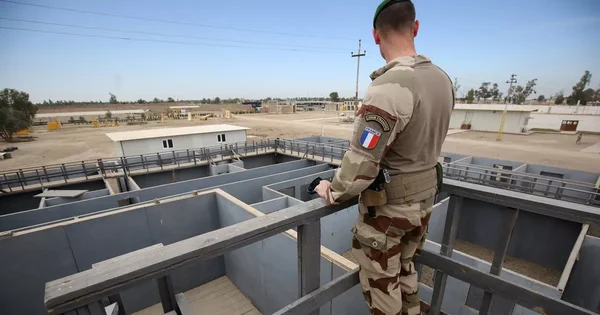 Des soldats en treillis et bérets alignés en formation, un autre soldat casqué faisant face au groupe.