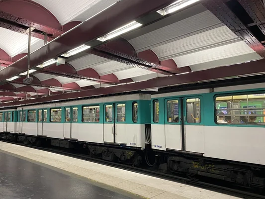 Rame l'arrt sous les poutres rouges de la station avec des passagers aux fentres.