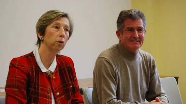 Deux personnes assises dans un intérieur, dont l'une porte une veste en carreaux.