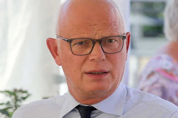 Édouard Philippe pose en costume devant un fond de feuillages.