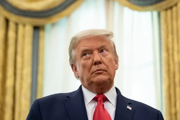 Donald Trump posant devant des rideaux dorés.