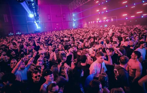 Atmosphère d'un concert ou festival avec foule et lumières bleues et violettes.
