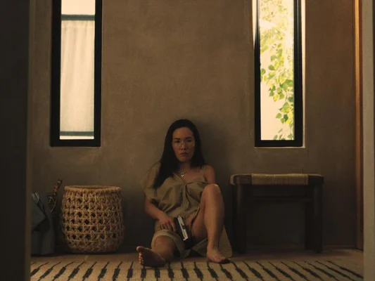 Une scène de la comédie noire Beef où une femme assise au sol tient une arme à feu.