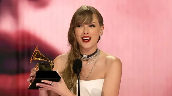 Taylor Swift tenant un trophée Grammy Award, vêtue d'une robe blanche bustier.