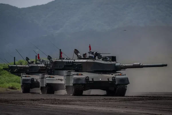 Trois chars de combat principaux manœuvrant dans un environnement montagneux et poussiéreux.
