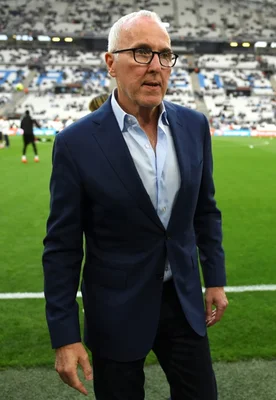 Un homme en costume et lanyard bleu debout dans les tribunes du stade.