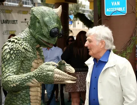 Sid Krofft interagissant avec un personnage en costume vert lors d'un événement.