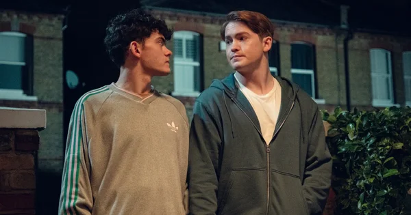 Joe Locke et Kit Connor partageant un moment complice devant un mur de briques dans la série Heartstopper.