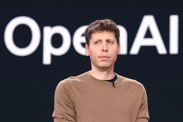 Sam Altman posant devant un fond sombre portant la mention OpenAI.