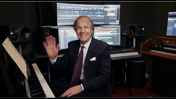 Richard Clayderman dans son studio d'enregistrement, souriant et saluant l'objectif.