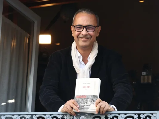 Kamel Daoud présentant son roman 'Houris' sur un balcon.