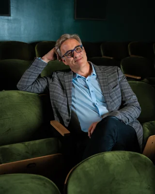 Michael Jackman détendu dans un fauteuil de cinéma, portant un blazer à carreaux.