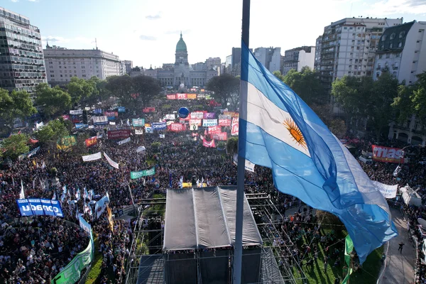Manifestation massive sur une place de Buenos Aires, avec un drapeau argentin en avant-plan.