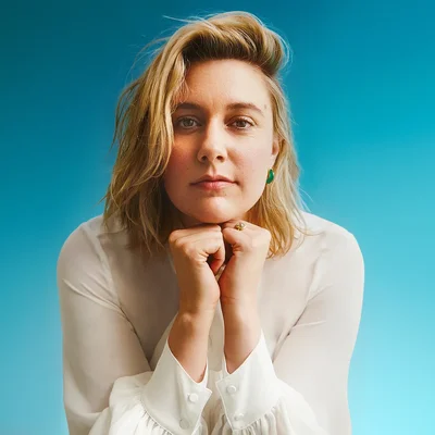 La réalisatrice Greta Gerwig posant pour un portrait avec un fond bleu.
