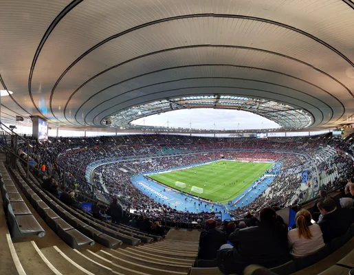 Vue du Stade de France depuis les gradins lors d'un match de football, avec son toit incurvé caractéristique.