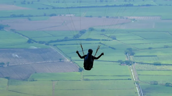 Parapentiste survolant des champs agricoles verts et bruns.