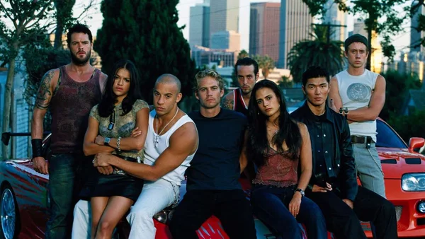 Le casting de Fast & Furious posant devant une voiture de sport rouge.