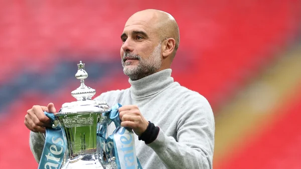 Pep Guardiola brandissant un trophée avec des rubans bleus.