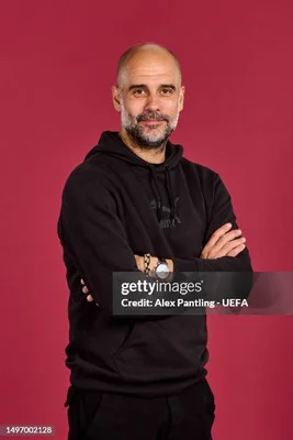 Portrait de Pep Guardiola en hoodie noir, bras croisés.