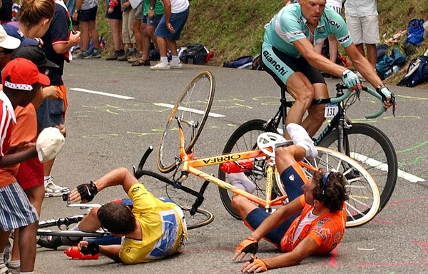 Deux coureurs à terre après une chute, observés par des spectateurs en bord de route.