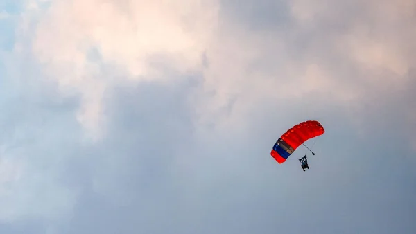 Personne descendant sous un parachute rouge, bleu et blanc dans un ciel nuageux.