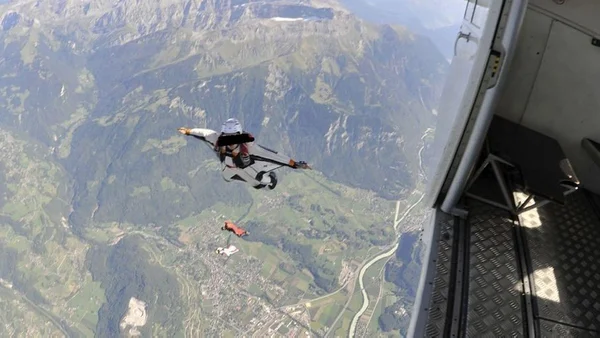 Des parachutistes en chute libre au-dessus d'une vallée montagneuse, après avoir sauté d'un avion.