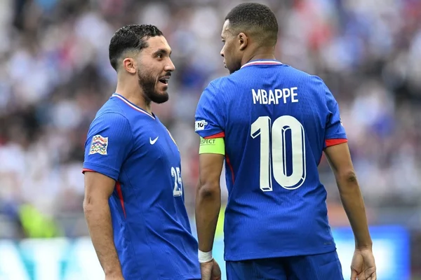 Kylian Mbappé et un coéquipier en discussion sur la pelouse lors d'un match des Bleus.