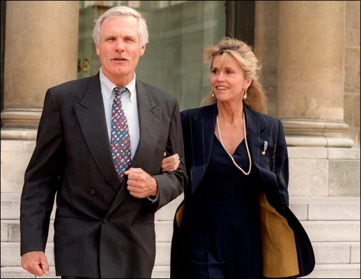 Ted Turner et une femme blonde, probablement son épouse, devant un bâtiment en pierre.
