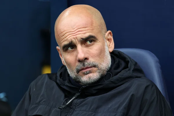 Pep Guardiola, regard sérieux, vêtu d'une veste à capuche noire.