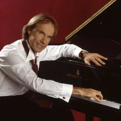 Richard Clayderman posant fièrement avec un piano Steinway & Sons.