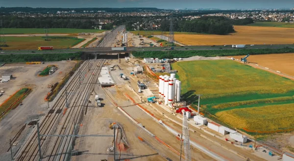 Vue aérienne du chantier ferroviaire du CDG Express avec voies, silos et engins près d'un pont autoroutier.