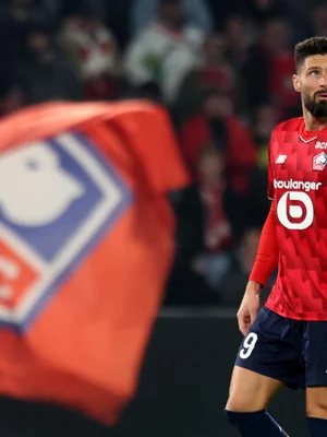 Olivier Giroud, portant le numéro 9, sur la pelouse avec un drapeau rouge en avant-plan.