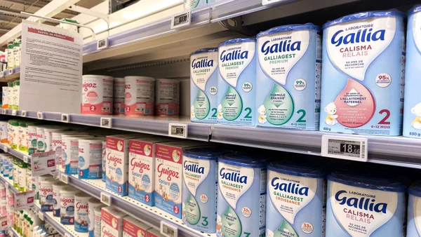 Rayon de laits infantiles en supermarché, avec un avis de rappel de produit visible à gauche.