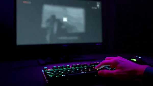 Main d'un joueur appuyant sur une touche de clavier avec un écran d'ordinateur affichant un jeu vidéo qui se fige et devient gris, ambiance sombre de chambre de joueur