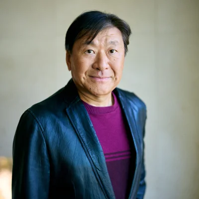 Koji Suzuki en pull violet et veste en cuir, photographié en plan moyen.